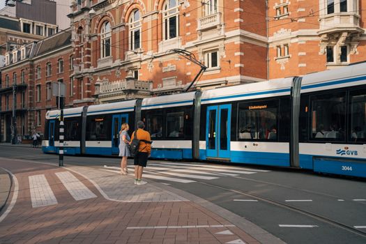 Tram on city street near International Theater in Amsterdam with pedestrians on crosswalk.