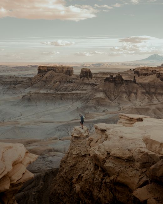 A man stands atop a dramatic sandstone cliff in Hanksville, showcasing breathtaking canyon views.