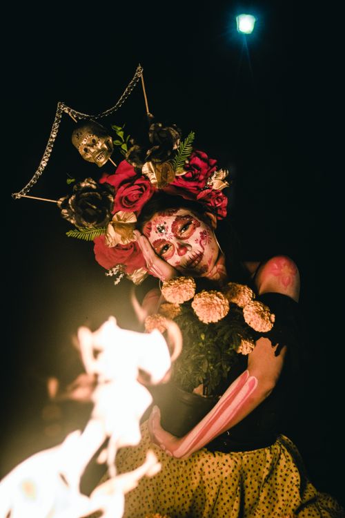 Free A woman with a painted face and floral wreath poses beside fire, embracing Mexican culture. Stock Photo