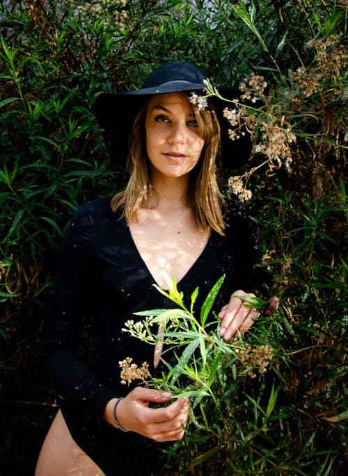 Portrait of Woman in Hat and Black Clothes among Bushes