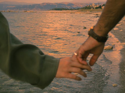 Close up of Couple Holding Hands on Sea Shore at Sunset
