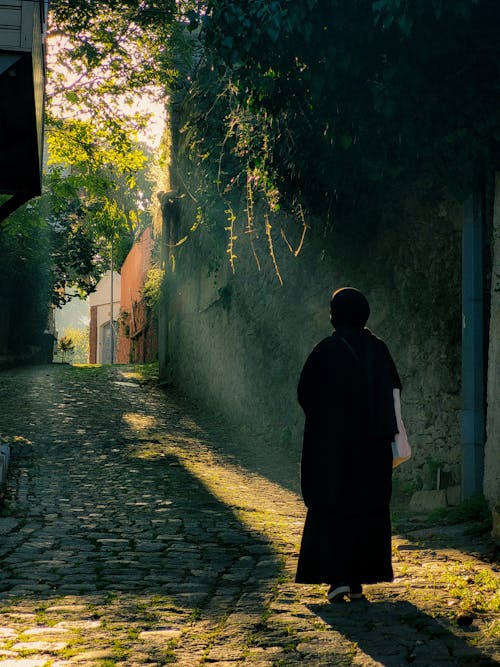 Back View of a Person Walking in a Cobblestone Alley 