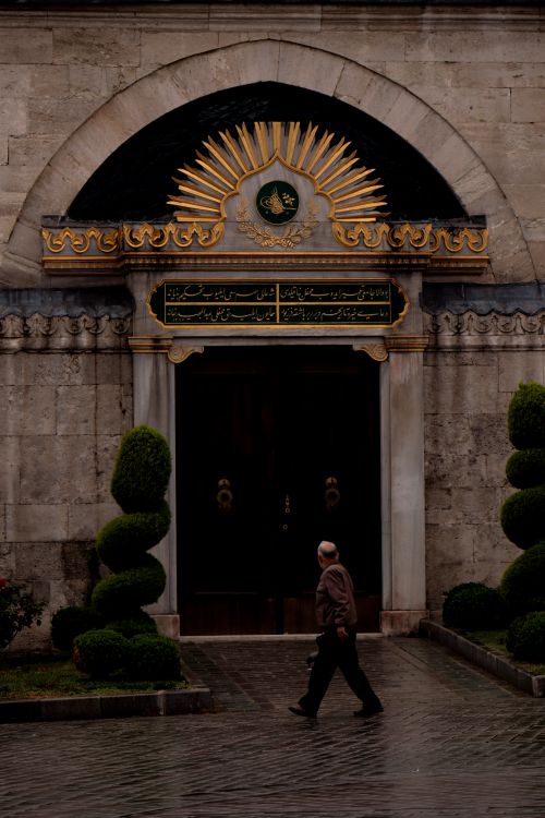 Free Man walking past a grand Ottoman entrance in Istanbul, capturing cultural elegance. Stock Photo