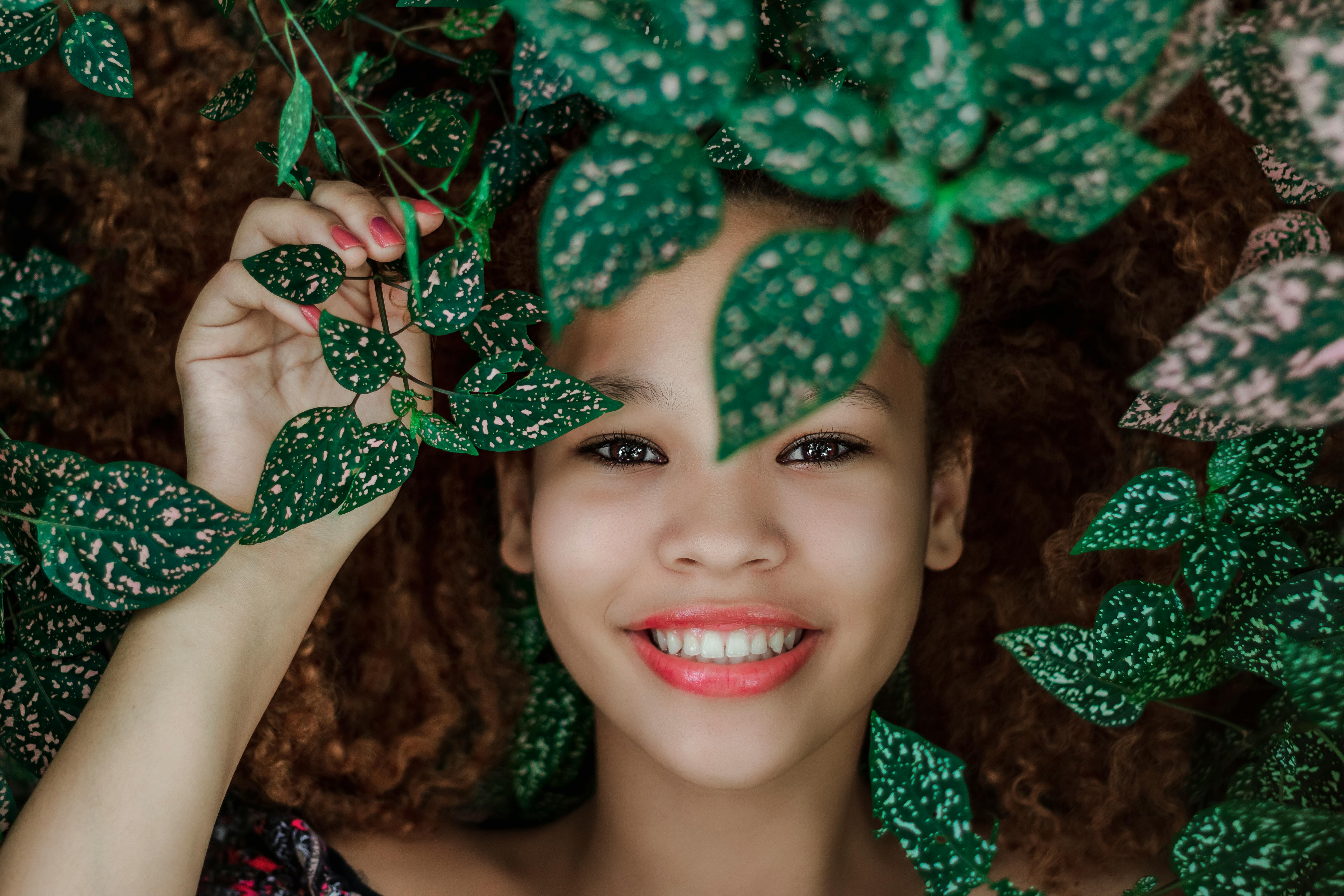 Portrait of a smiling woman surrounded by vibrant leaves, showcasing natural beauty.