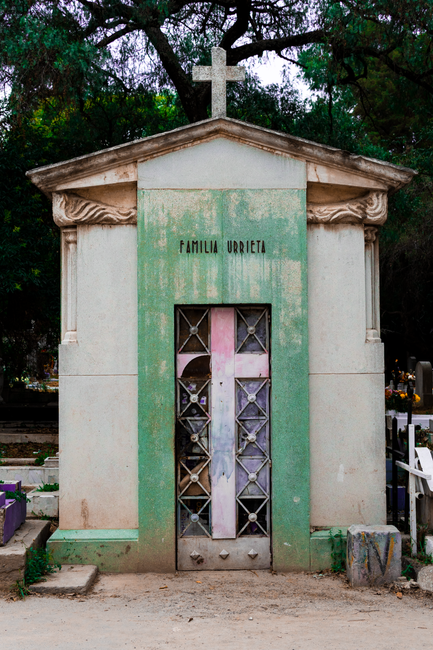 Fotomural Una antigua tumba familiar con una cruz en un cementerio de la Ciudad de México, rodeada de vegetación.