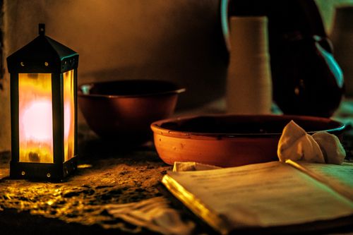 Free Warm and inviting scene featuring a glowing lantern, open book, and clay bowl. Stock Photo