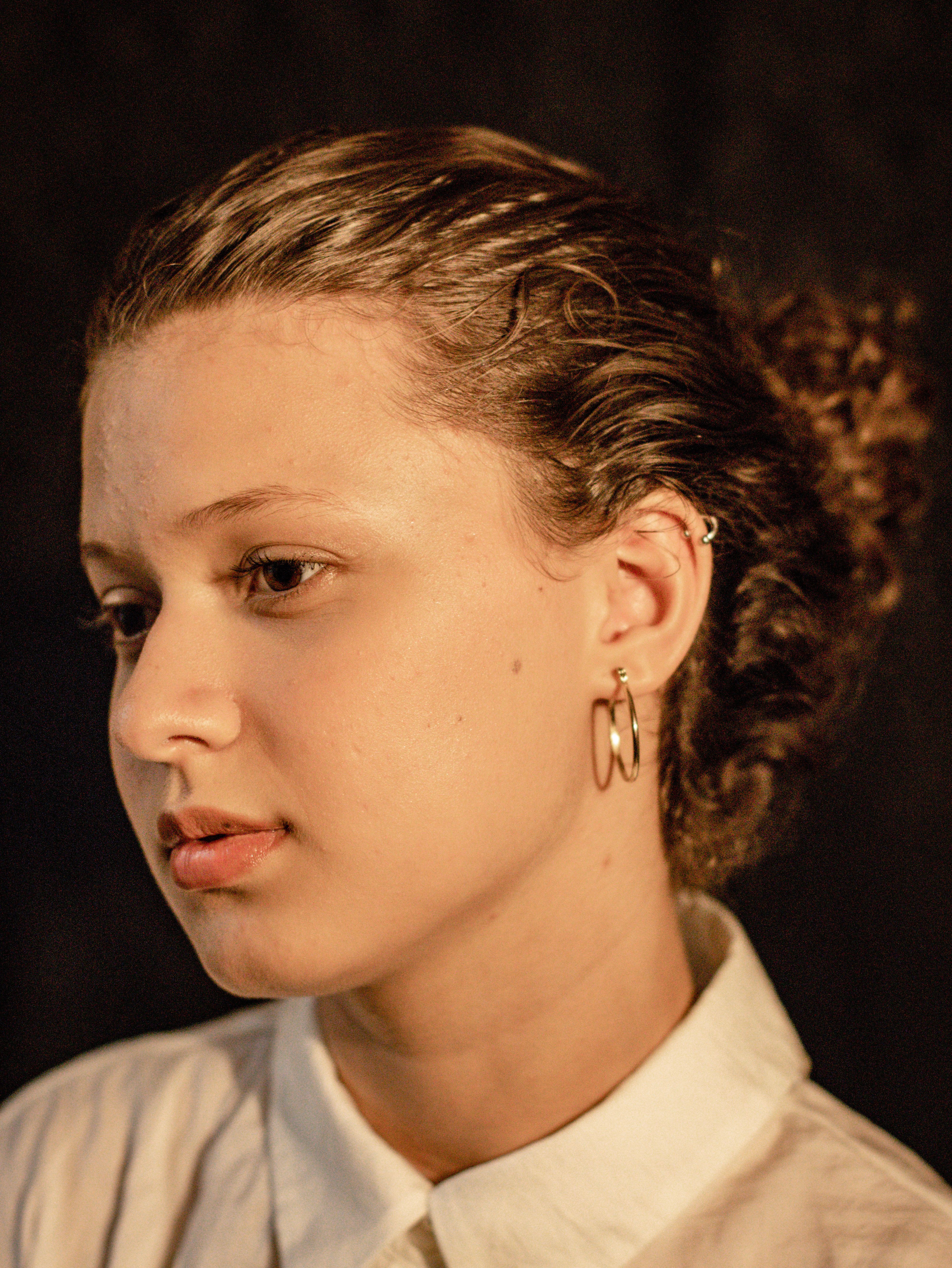 Profile portrait of a serene young woman with curly hair and hoop earrings.