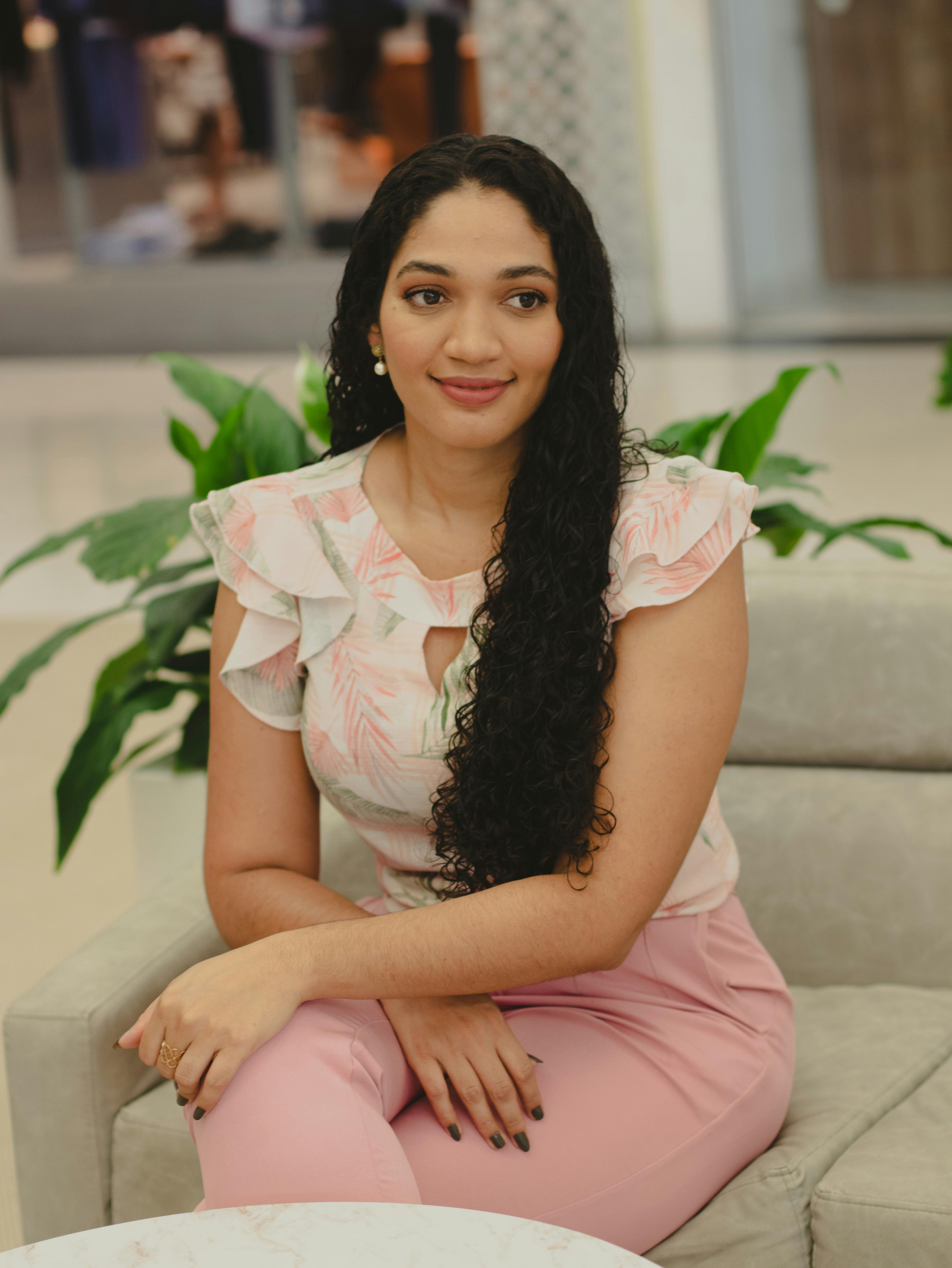 Portrait of a smiling woman with long black hair sitting elegantly indoors.