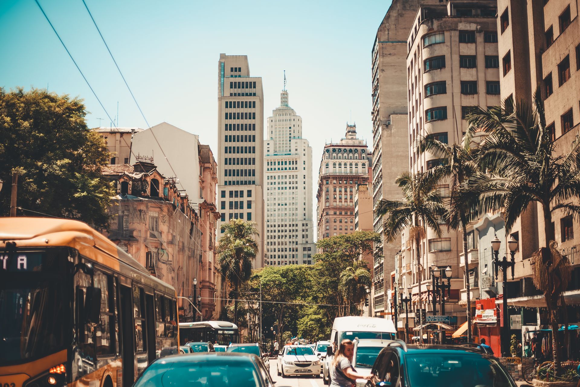 Street view of a busy city with towering skyscrapers and bustling traffic under clear skies.