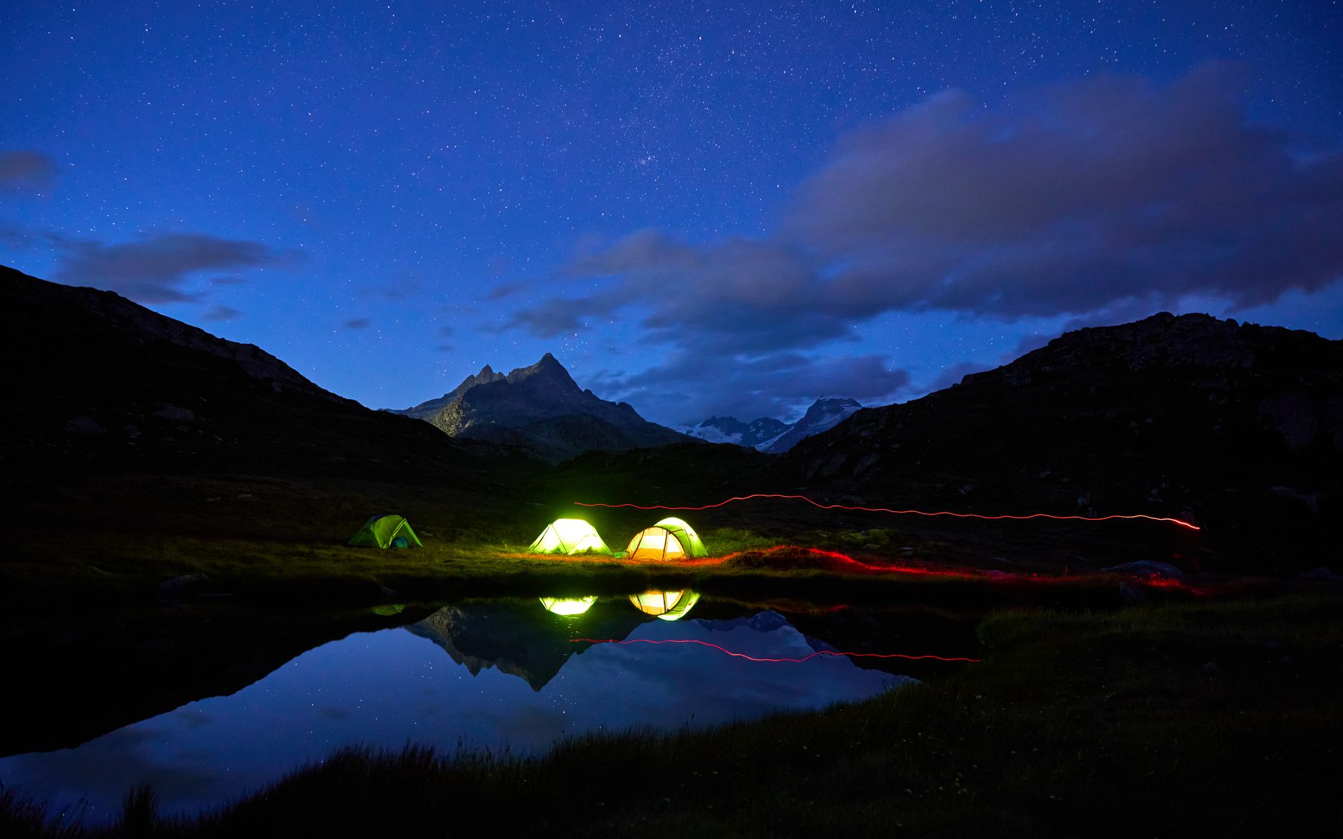 Beautiful night camping scene with tents under starry sky and mountain reflections in a lake.