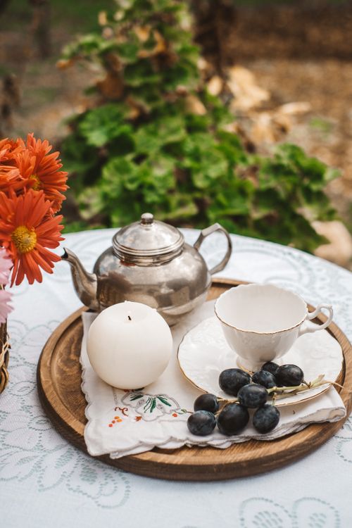 Free A vintage tea pot and cup set with grapes on a tray, beautifully adorned with flowers, in an outdoor setting. Stock Photo