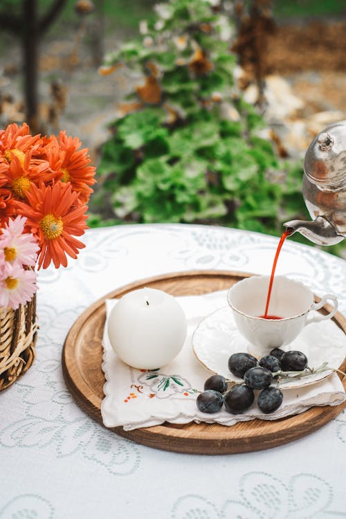 Pouring Beverage to Cup on Plate on Tray with Fruit and Wax Candle