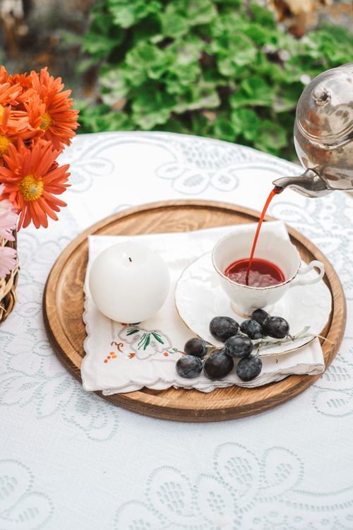 Free An elegant tea setup on a lace tablecloth with a teacup, grapes, and vibrant orange flowers. Stock Photo