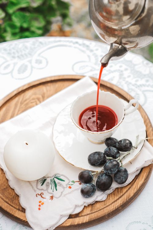 Free A serene table setting with tea being poured, accompanied by fresh grapes and a candle on a wooden tray. Stock Photo