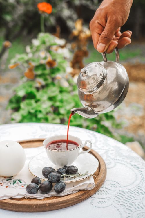 Free A hand pours tea into a teacup next to grapes on a garden table. Stock Photo