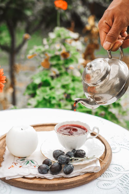 Hand Holding Kettle and Pouring Drink to Cup on Tray