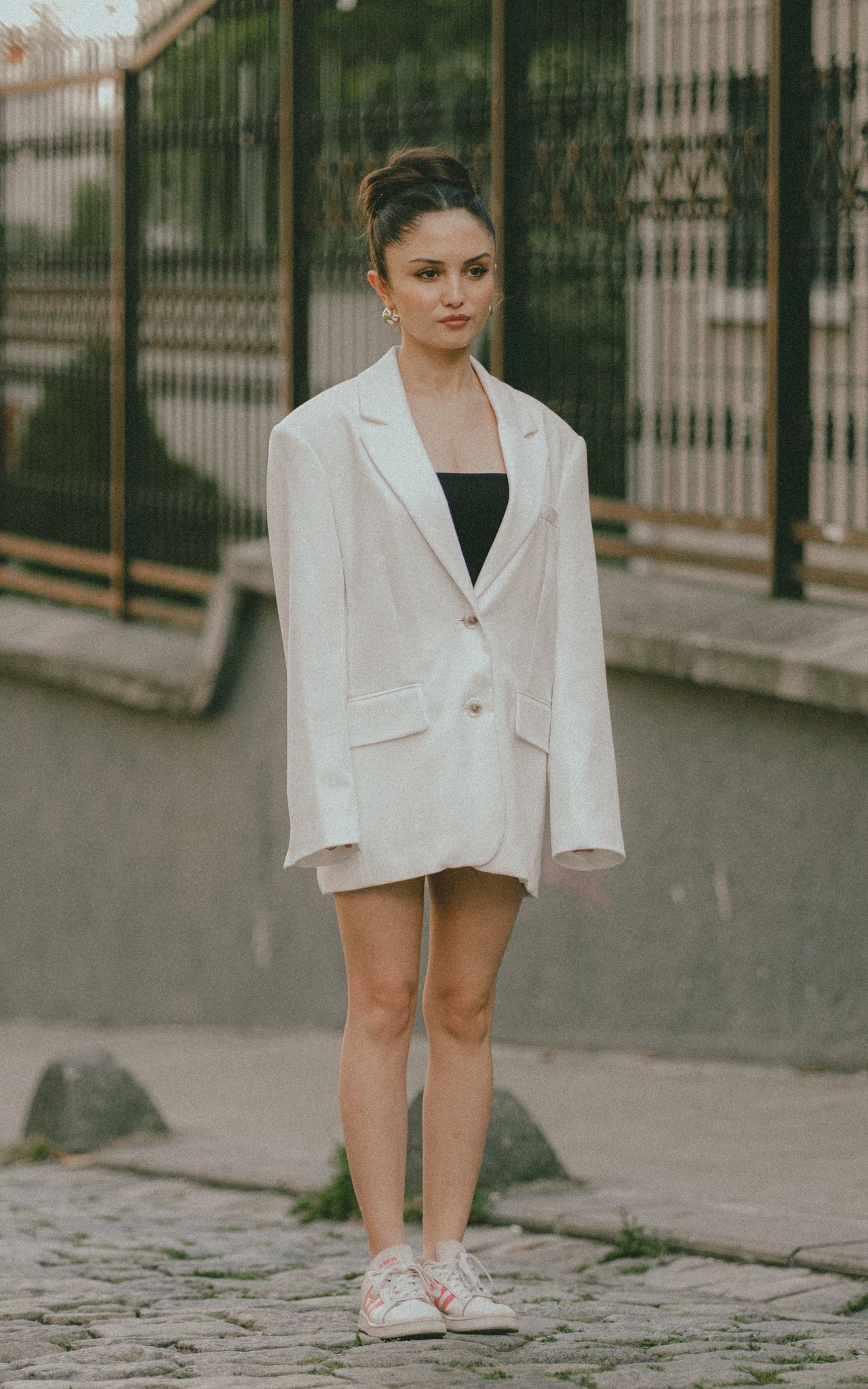 Woman in an oversized white blazer and sneakers on a cobblestone street