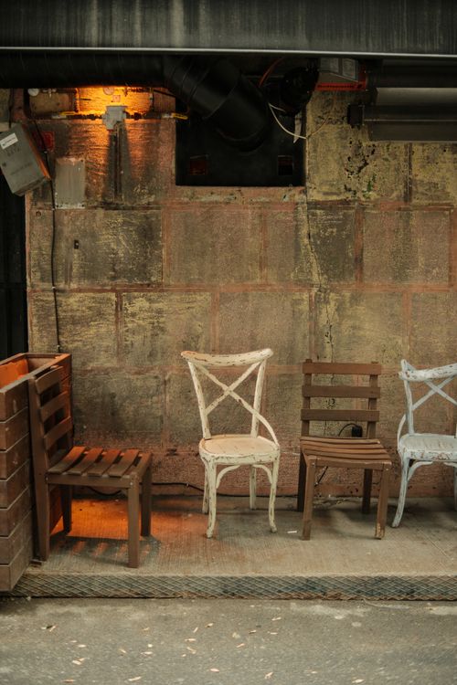 Free Three rustic chairs against a textured, industrial-style wall illuminated with warm lighting. Stock Photo