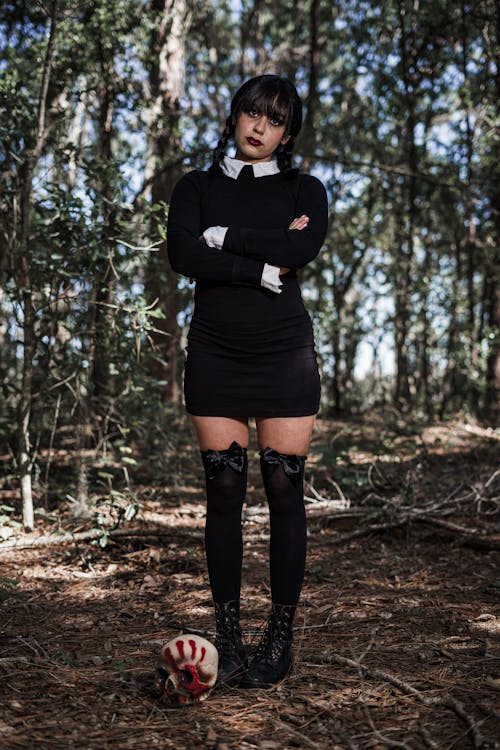 Girl Dressed as Wednesday Addams for Halloween Standing in the Forest 