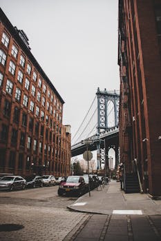曼哈顿大桥的经典景观，被布鲁克林的红砖建筑环绕，周围停放着汽车
