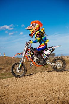 Young racer on a dirt bike with helmet and gear, speeding on a gravel track.
