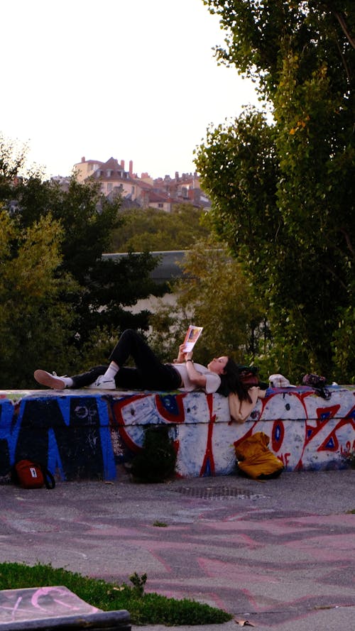 Woman Lying Down on Wall with Graffiti and Reading Book