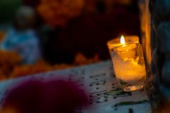 A warm candle illuminates a Dia de Muertos altar with marigold flowers and a serene ambiance.