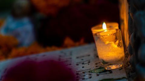 A warm candle illuminates a Dia de Muertos altar with marigold flowers and a serene ambiance.