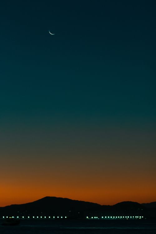 Free Crescent moon shining above hills at sunset with a glowing horizon. Stock Photo