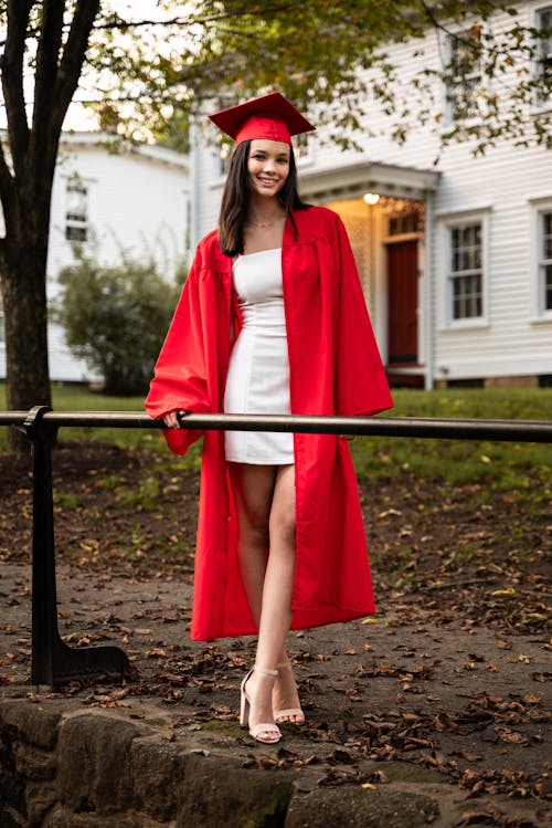 Smiling Graduate Standing in Red Gown and Academic Hat