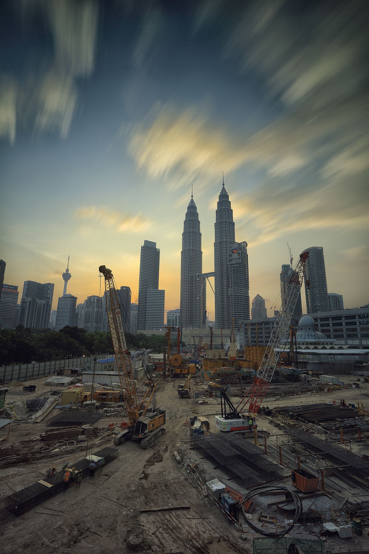 Yellow tower crane over a busy construction site in Kuala Lumpur, Malaysia, with the Petronas Towers behind