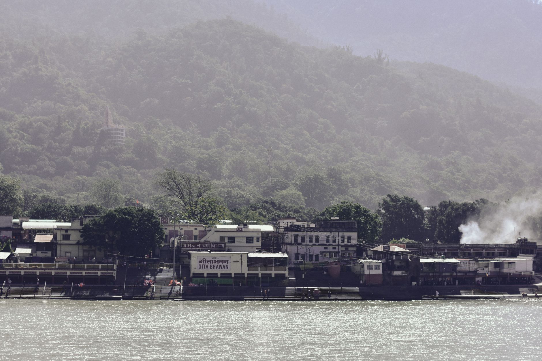 View of a tranquil riverside village with dense green hills in the background, ideal for travel and nature scenes.