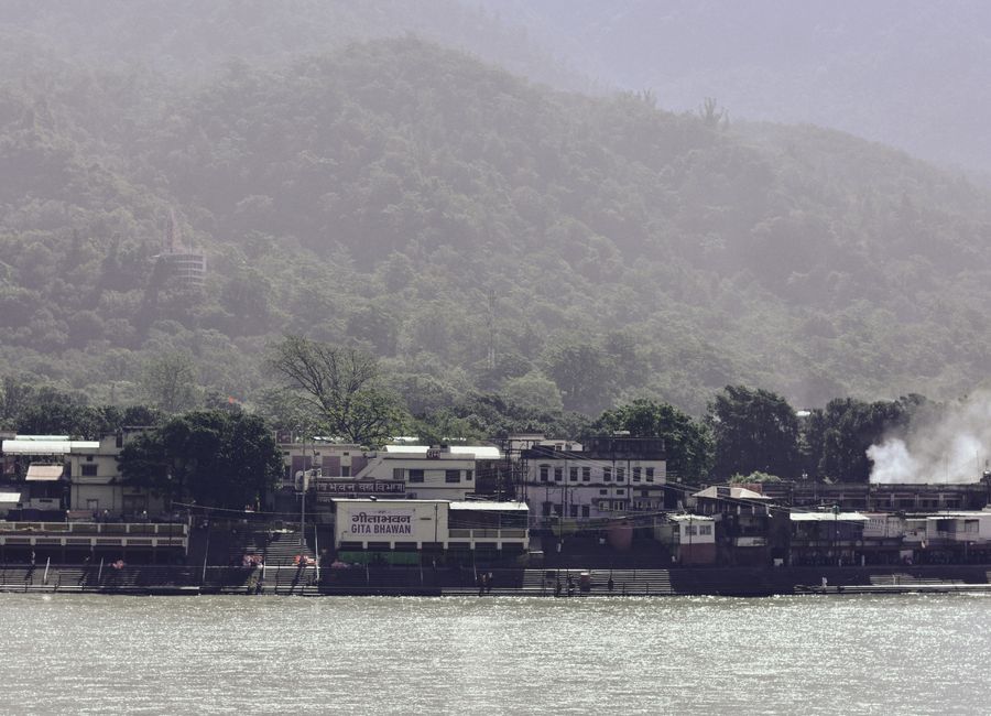 View of a tranquil riverside village with dense green hills in the background, ideal for travel and nature scenes.