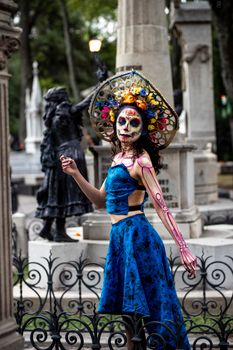 Vibrant portrait of a woman in traditional Dia de los Muertos attire, posing in a graveyard.
