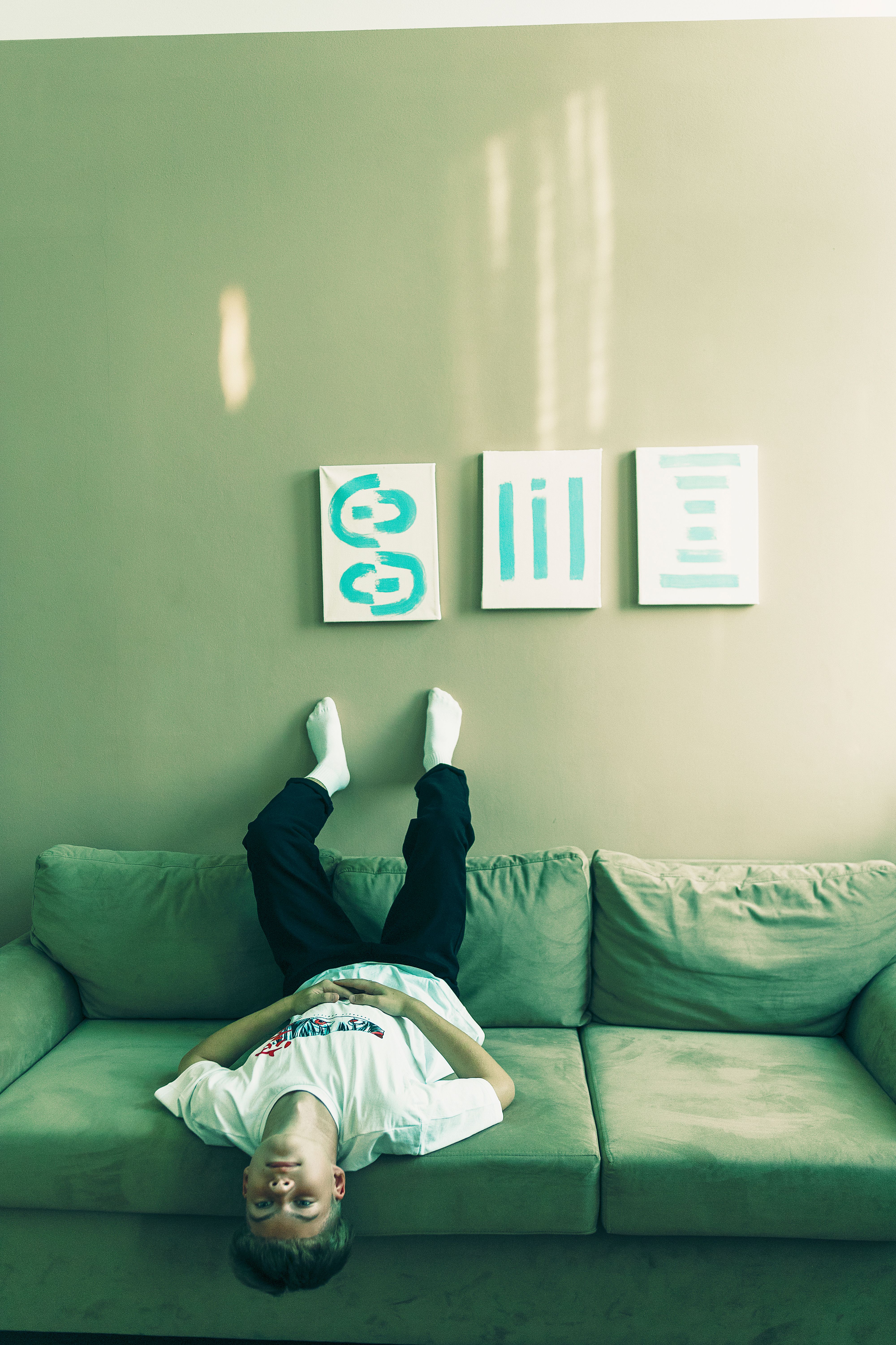 Young man relaxing upside down on a sofa with art on walls in a modern interior.