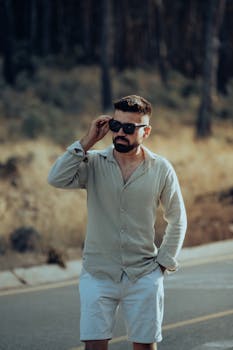 Man in casual outfit wearing sunglasses on a rural road, embodying a relaxed summer vibe.