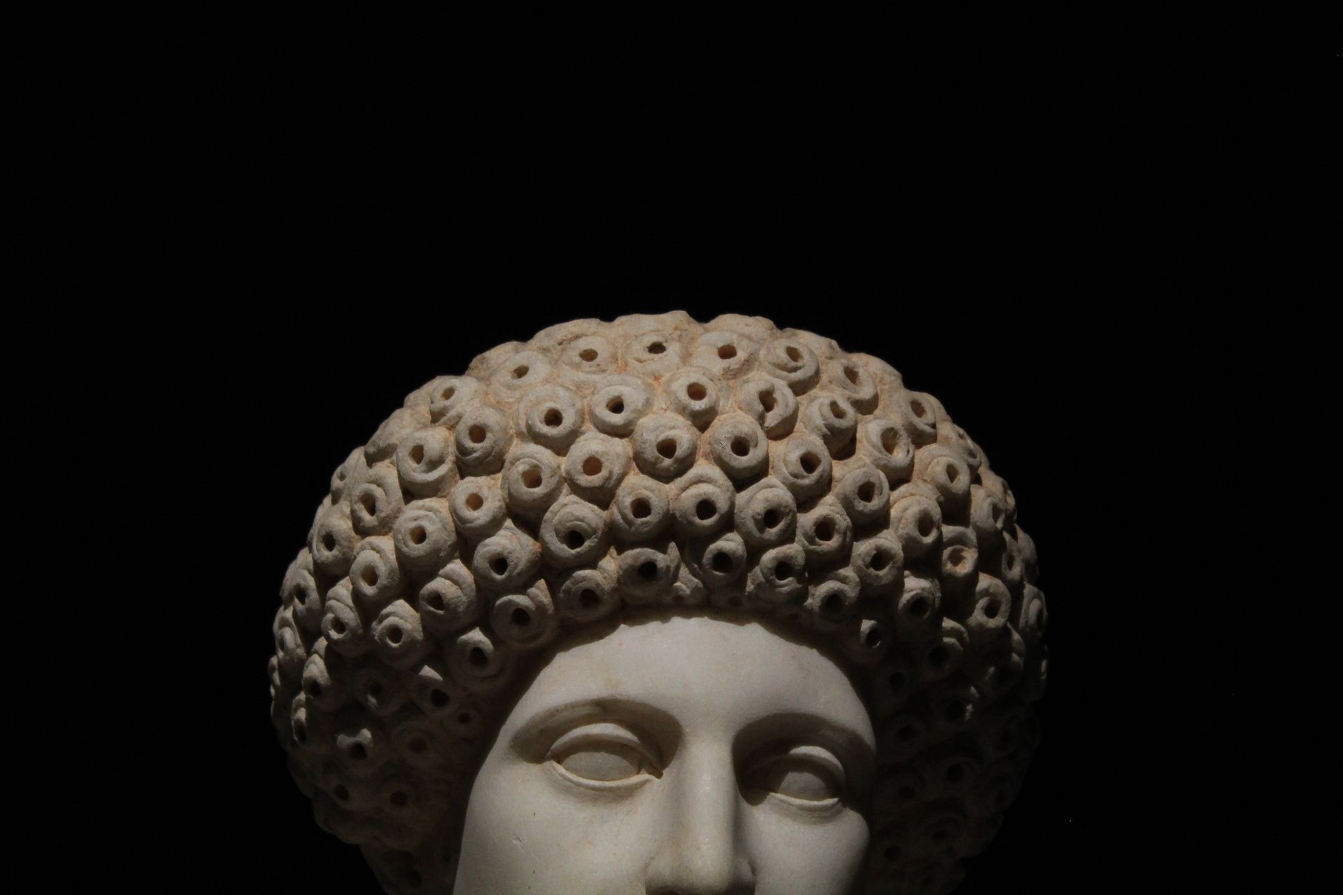 Detailed close-up of a Roman marble sculpture's bust with intricate hair on a black background.