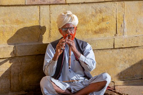 Free South Asian man playing double flute against sandstone wall in Udaipur. Stock Photo
