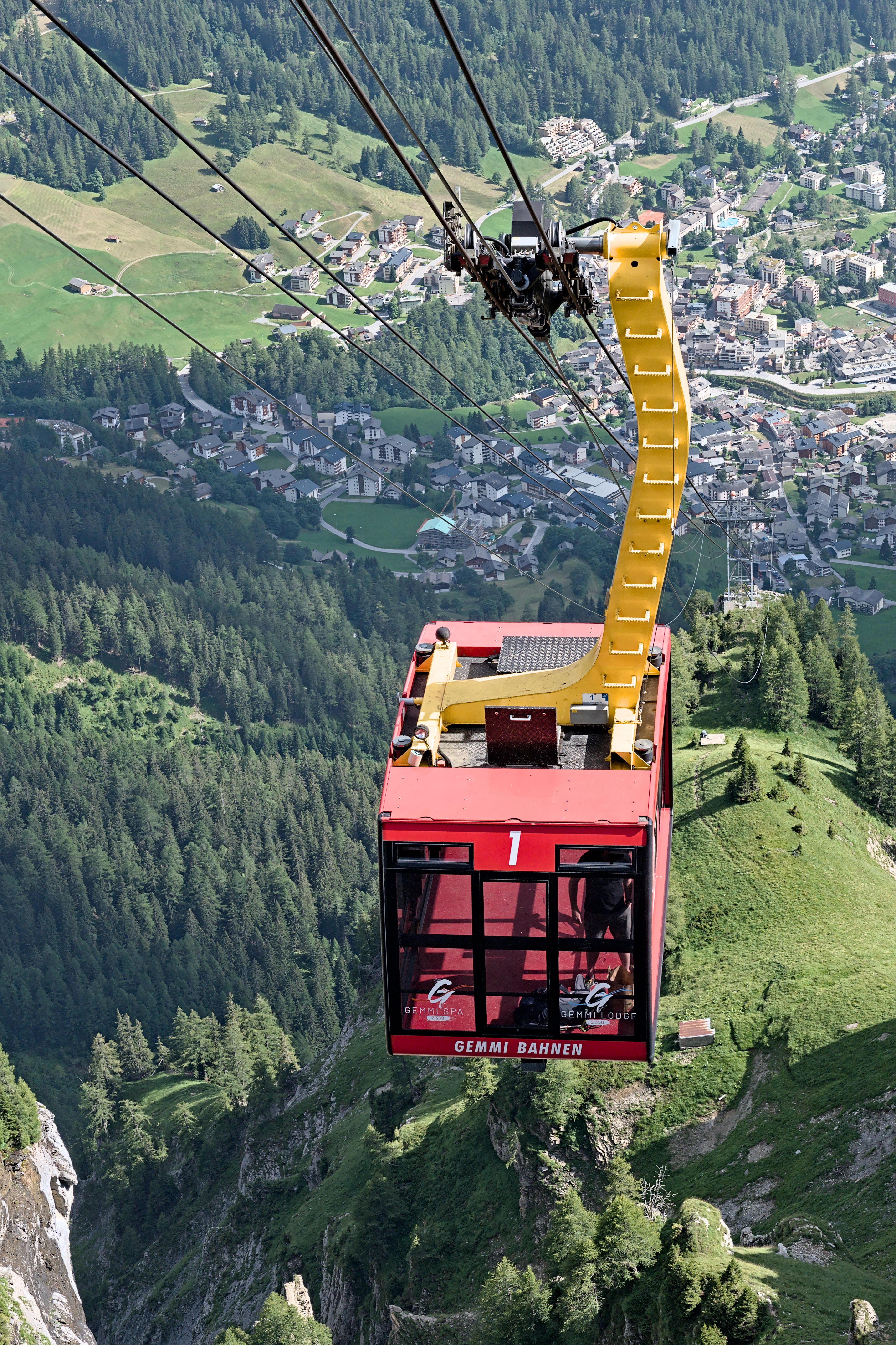 A red Gemmi Bahn cable car travels over Leukerbad, offering a breathtaking mountain view.
