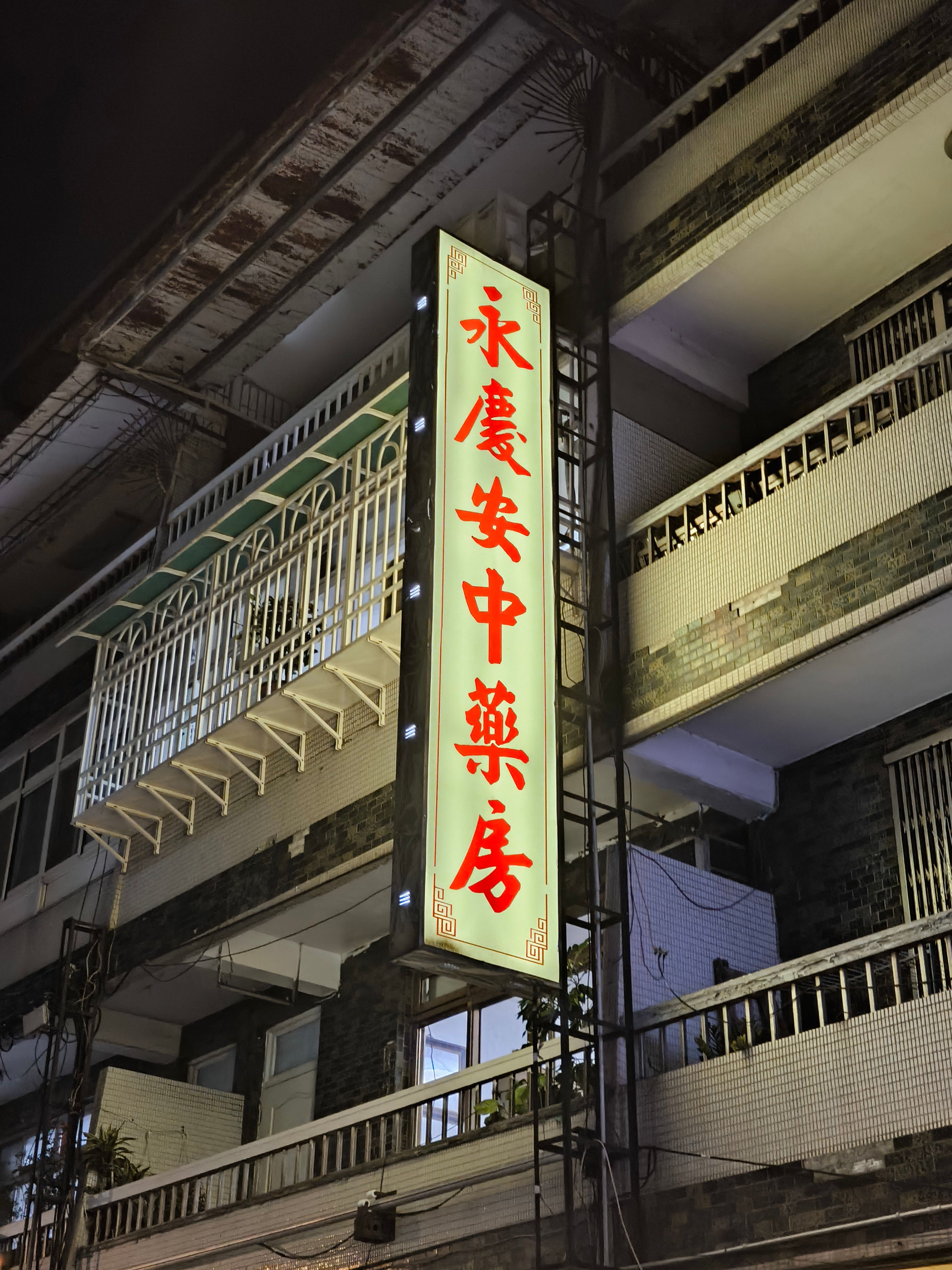 Urban building facade with neon Chinese sign at night, featuring balconies and city atmosphere.