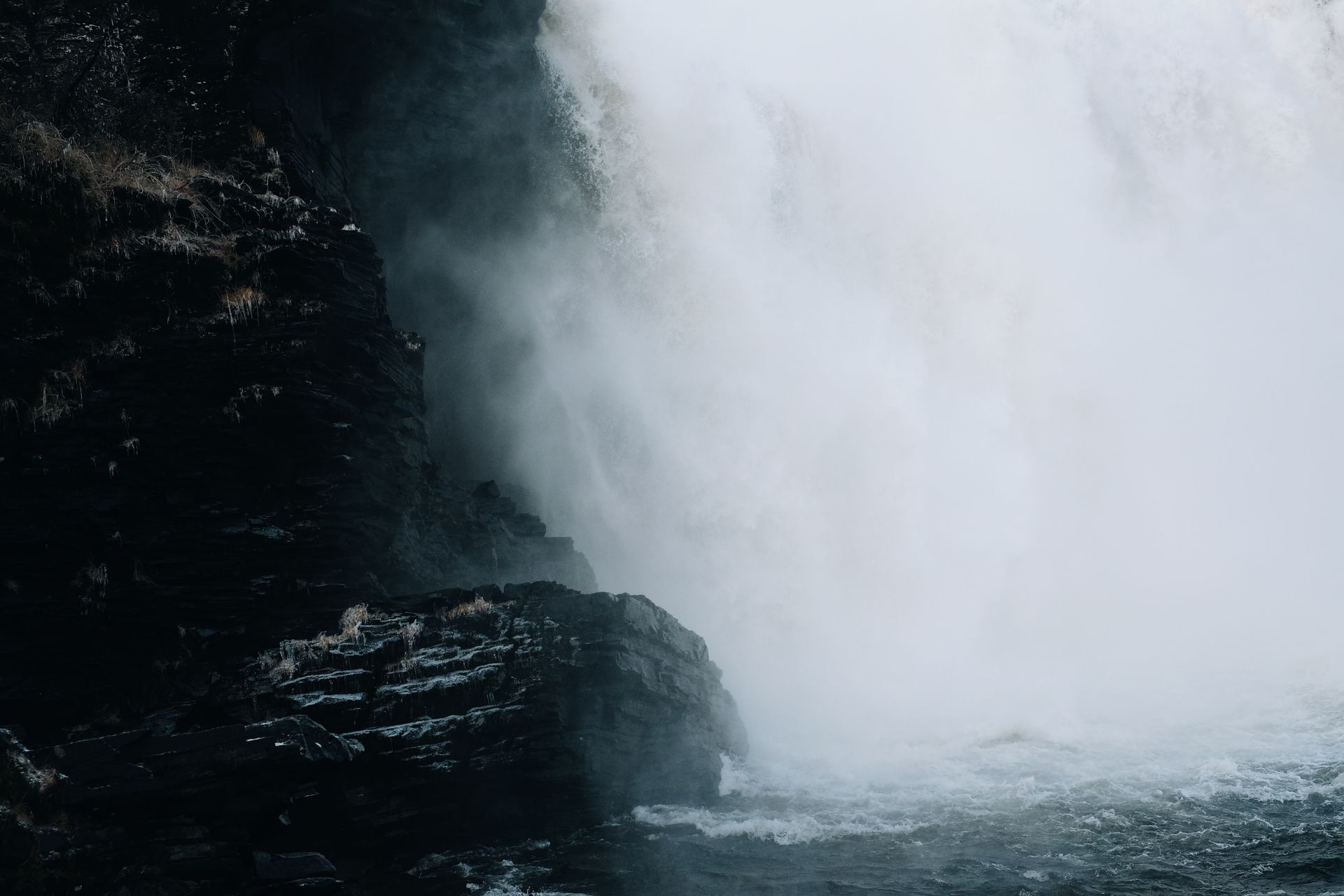 Moody waterfall with dramatic mist cascading over dark rocky cliffside.