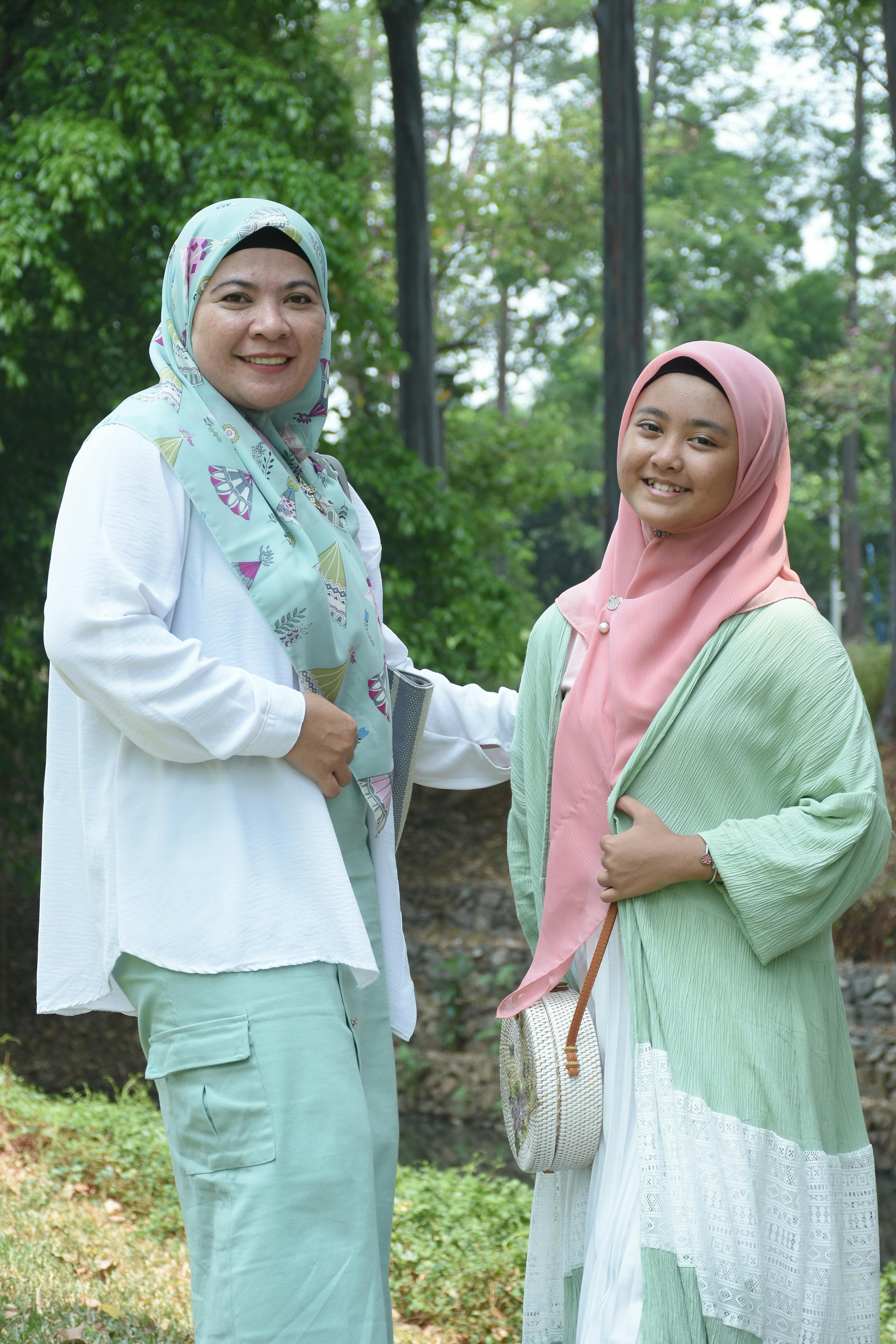 A cheerful mother and daughter smiling together outdoors in a lush green setting.