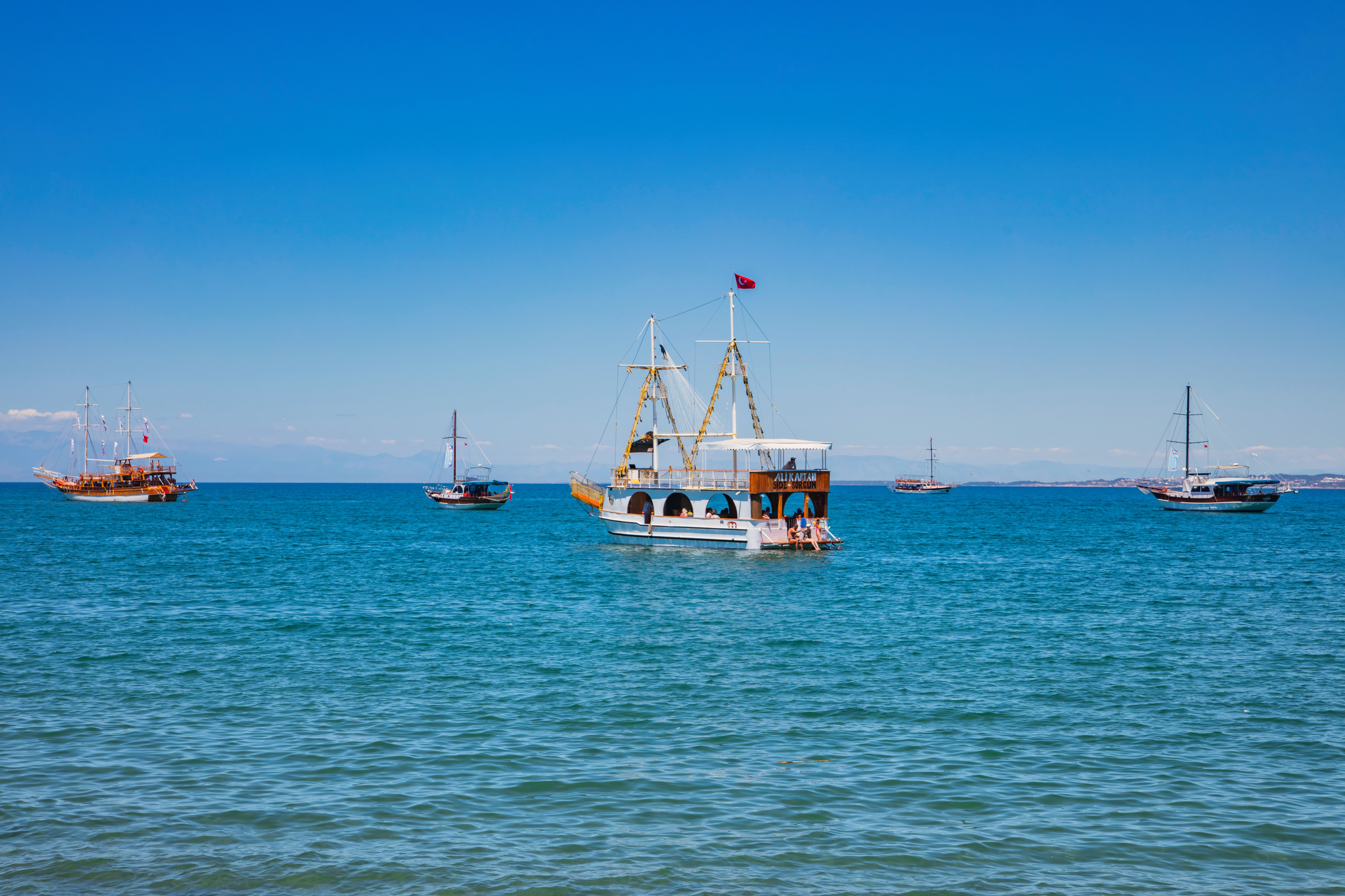 Unforgettable Alanya All Inclusive Yacht Tour With Hotel Transfer Review 2026 - Boats sailing on the clear blue waters of Side, Antalya, under a bright summer sky.