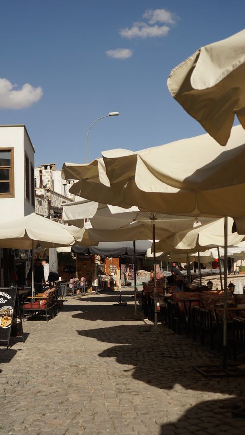 Free Cobblestone street outdoor cafe with tables and umbrellas under a clear blue sky. Stock Photo