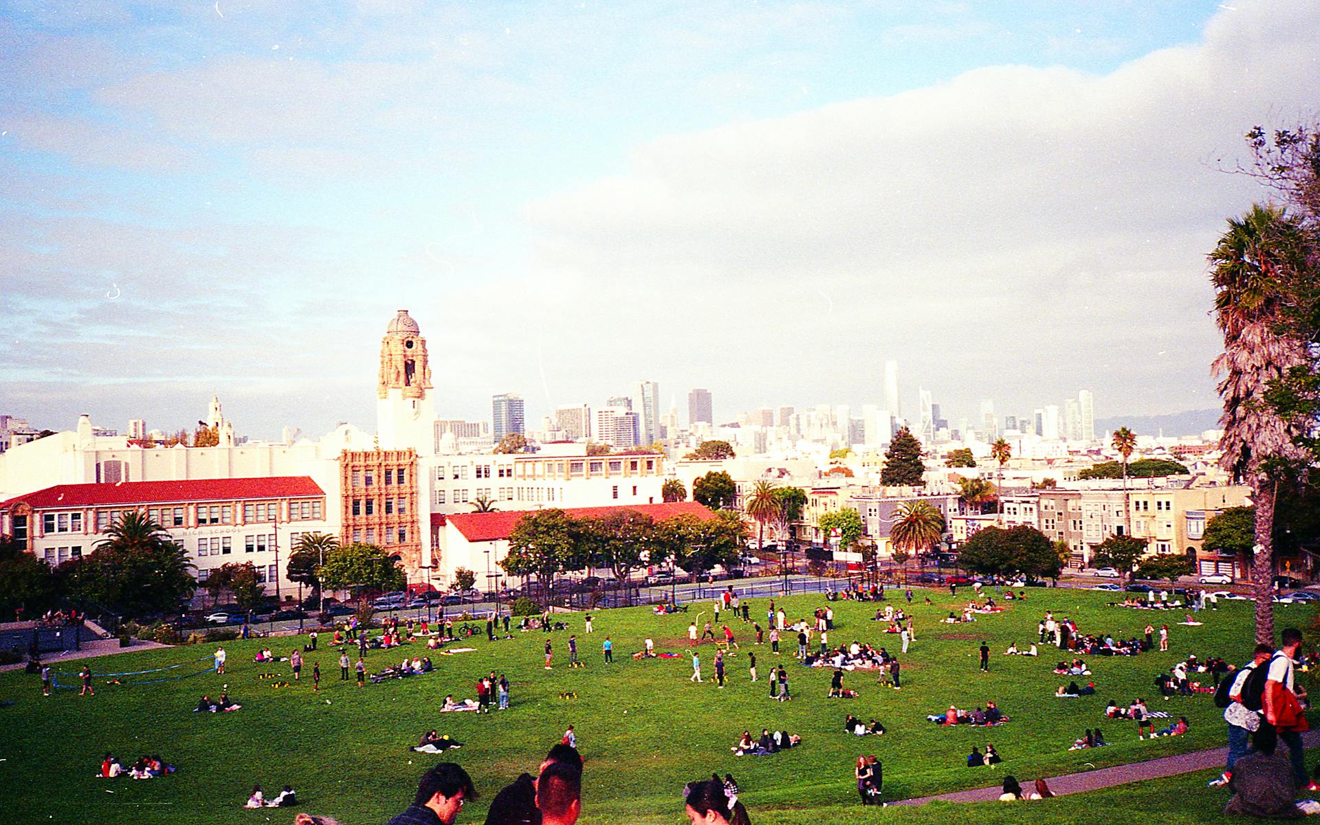 People enjoying a sunny day at Dolores Park with San Francisco skyline views.