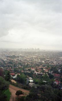 Aerial perspective of Los Angeles cityscape under cloudy skies, showcasing urban sprawl and skyline.