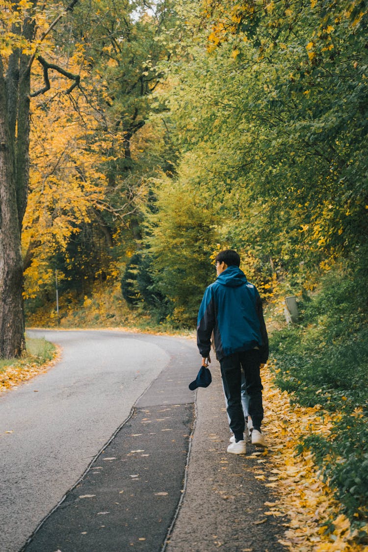 Young Man Walking Uphill Along A Road By The Forest