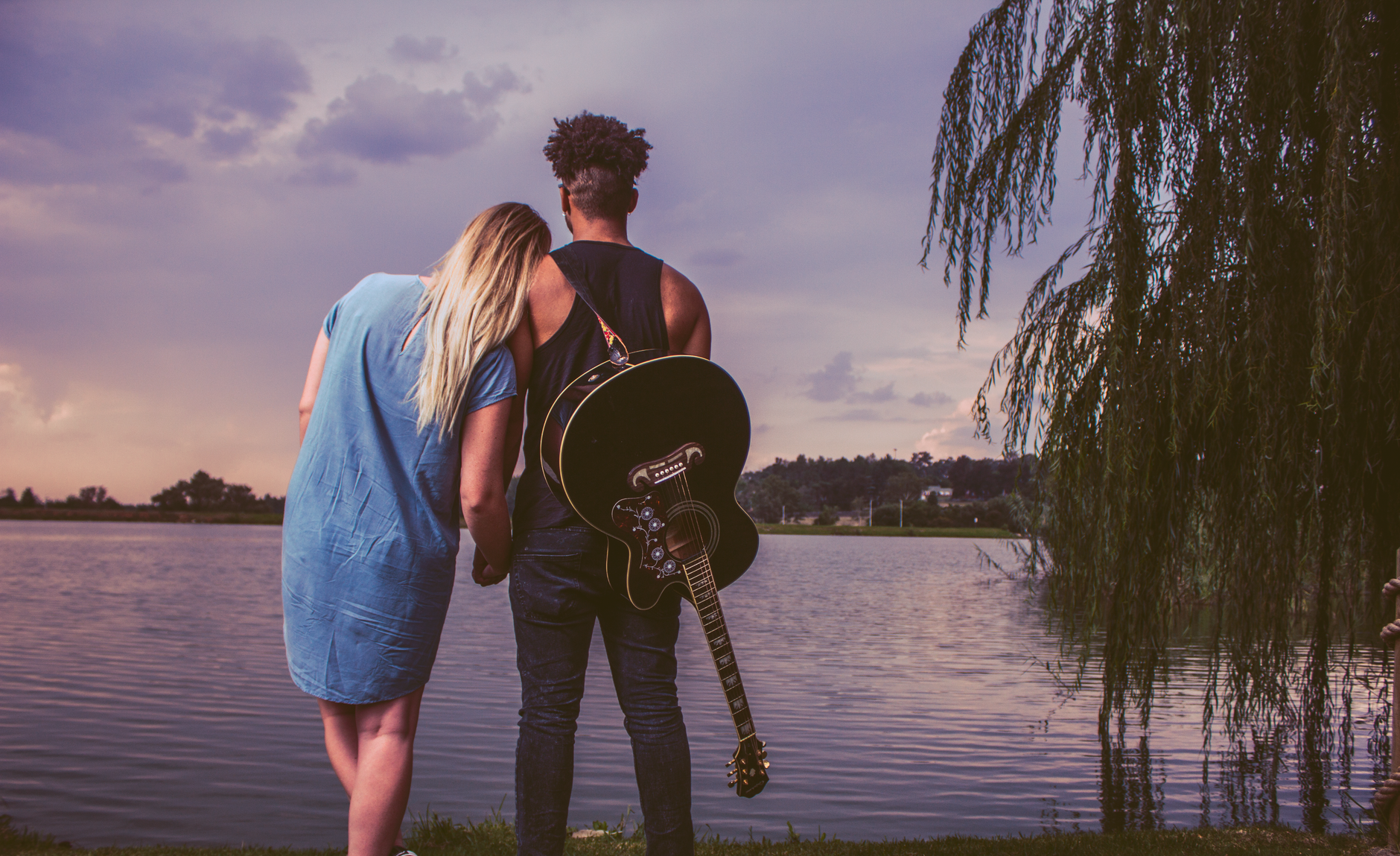 A couple embracing by a tranquil lake with a guitar, creating a serene and romantic mood.