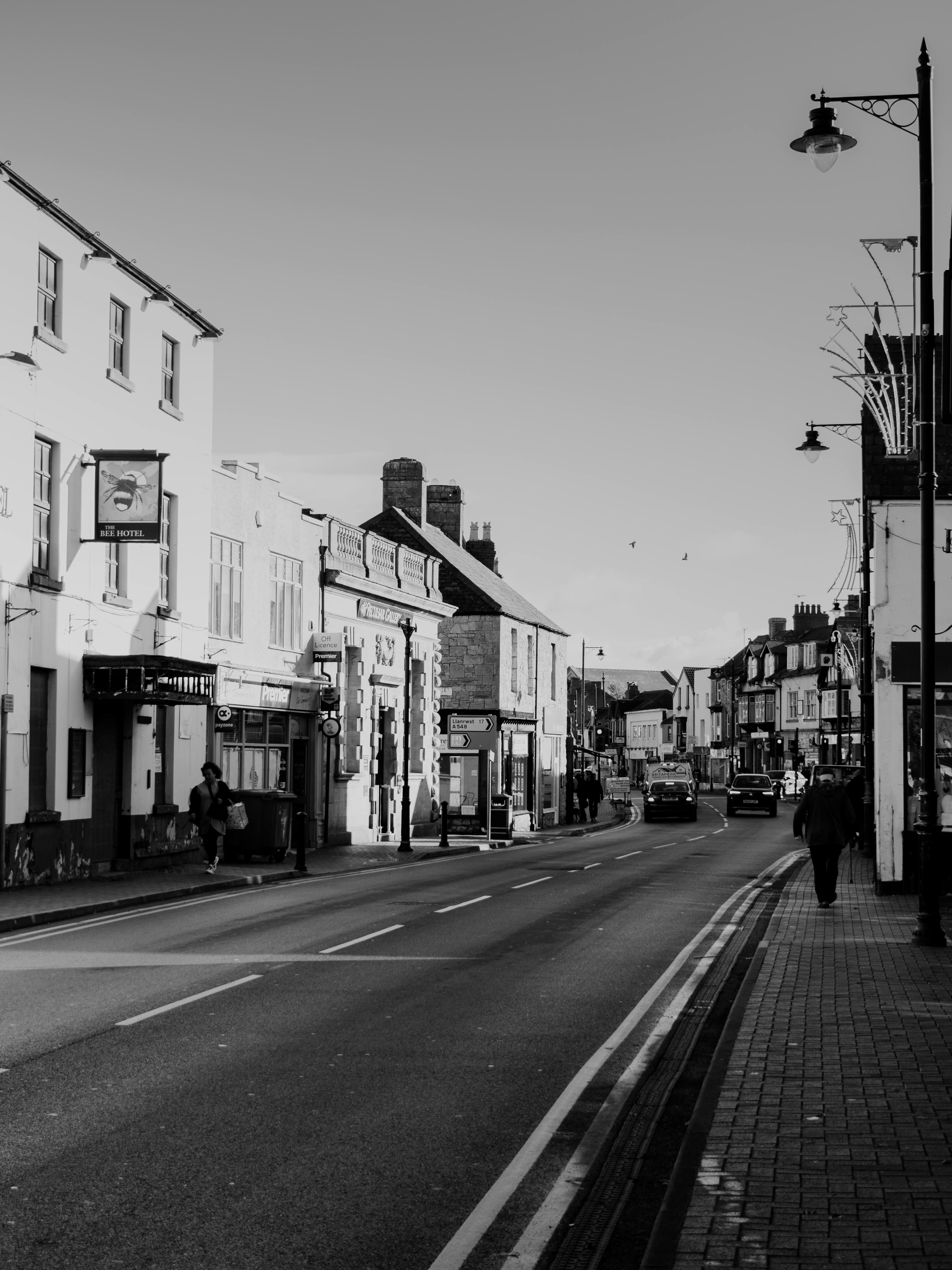 A moody black and white photo of a quiet urban street with classic architecture and few pedestrians.