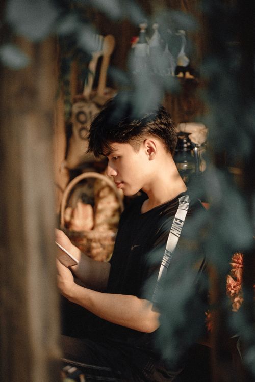 Free A thoughtful teenager in a black t-shirt reads indoors in warm lighting. Stock Photo